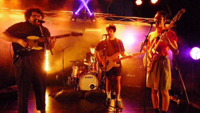 Un groupe de rock en concert sous les lumières orange et violettes - photo AMAC / Les Mouillotins