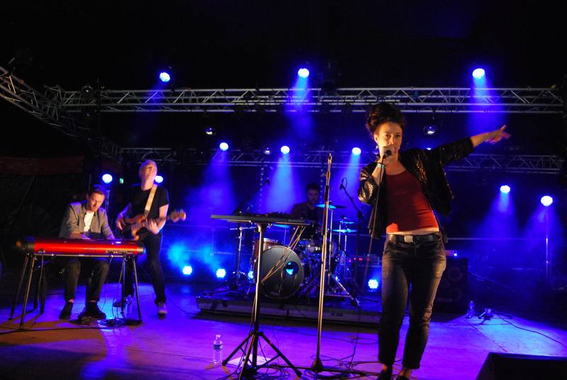 Une chanteuse et son groupe sur scène sous les lumières bleues - photo AMAC / Les Mouillotins