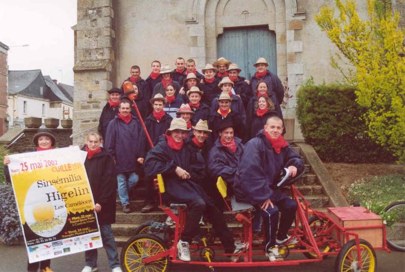Les Mouillotins en costume sur leurs vélos devant l'église, avec l'affiche Higelin et Sinsémilia - photo AMAC / Les Mouillotins