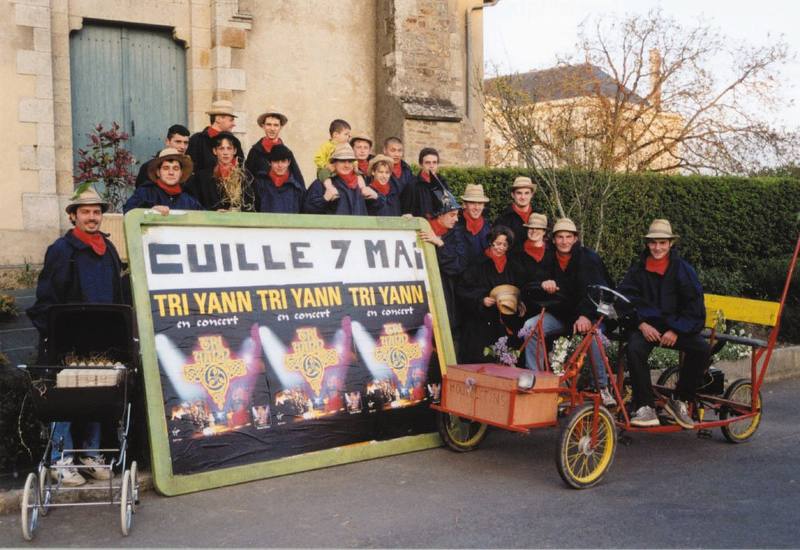 Les Mouillotins en costume devant l'église de Cuillé avec la banderole annonçant Tri Yann à Cuillé le 7 mai - photo AMAC / Les Mouillotins