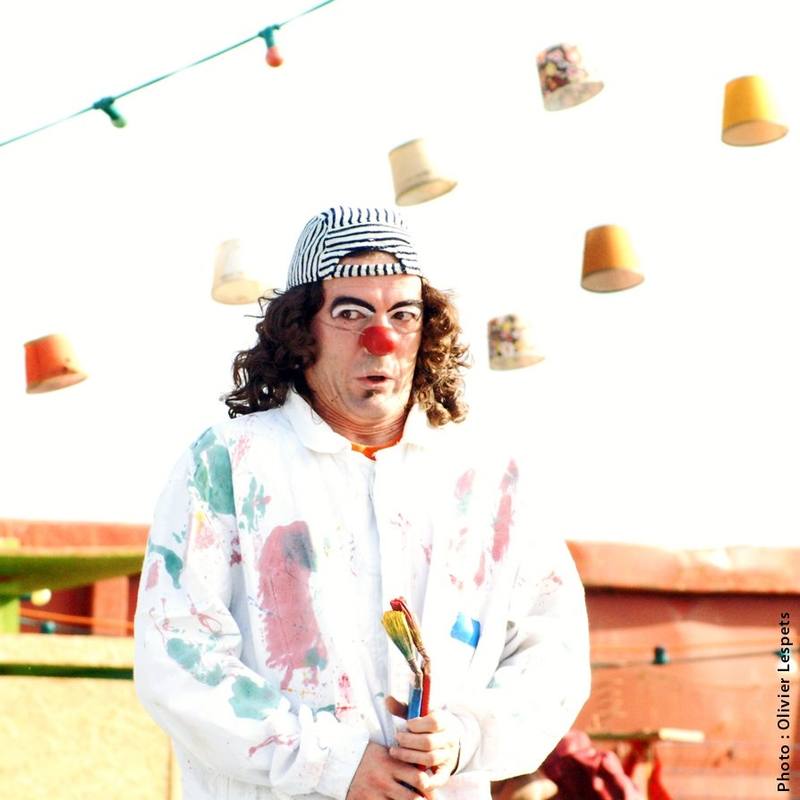 Un clown de la Cie Talisao, pinceau à la main, sous les guirlandes de pots - photo Olivier Lespets
